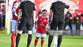 A smiling Saints mascot standing between skipper Ian Bermingham and referee Rob Hennessy ahead of the Athletic's 4-0 win over City last April