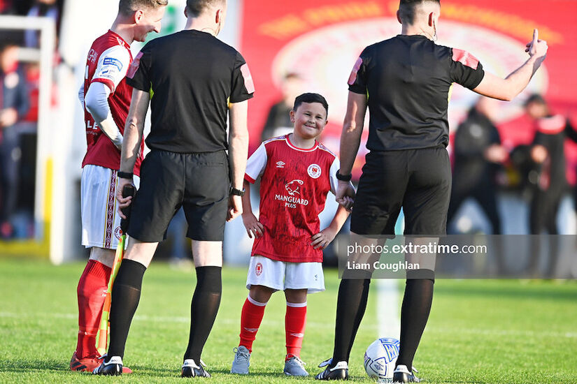 A smiling Saints mascot standing between skipper Ian Bermingham and referee Rob Hennessy ahead of the Athletic's 4-0 win over City last April